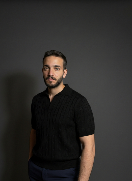 Man wearing a black polo shirt against a dark background